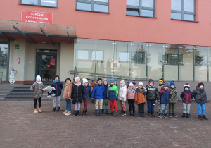 Przedszkolaki z misiem przed wejściem do budynku szkoły