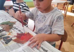 02. Chłopiec maluje liścia farbami.