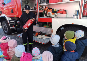 Strażak prezentuje dzieciom wyposażenie wozu strażackiego