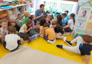 dzieci siedzą na podłodze skupione wokół prowadzącego
