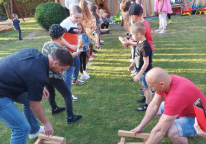 42 Dzieci i rodzice podają sobie drewniane klocki i budują z nich krzesła