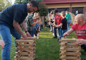 43 Dzieci i rodzice podają sobie drewniane klocki i budują z nich krzesła