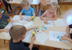Dzieci siedzą przy stoliku i malują palcami kropeczki na kartce