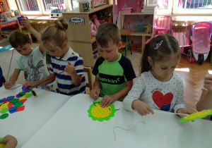 07 Dzieci nawlekają sznurki na kolorowe kwiatki z materiału.