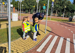 Pan Policjant pokazuje dzieciom jak prawidłowo przechodzić przez przejście dla pieszych.