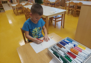 Chłopiec rysuje mazakami rysunek na papierze.