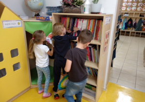 Dzieci wybierają książki z biblioteczki przedszkolnej.