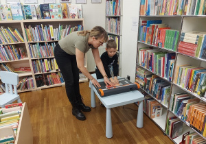 Chłopiec za pomocą specjalnej maszyny zakłada okładkę na książkę.