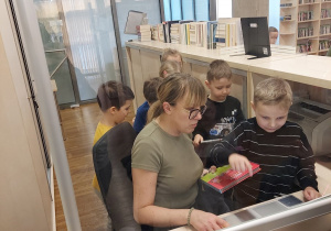 Pani bibliotekarka pokazuje dzieciom jak wypożycza się książki.