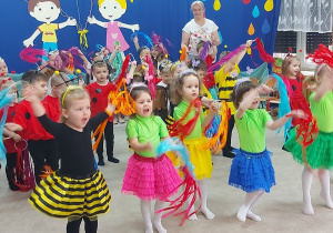 Dzieci ustawione w rzędach tańczą z kolorowymi chustkami