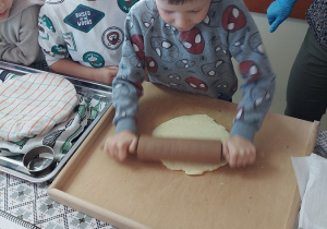 26. Chłopiec wałkuje ciasto na pierogi z serem.
