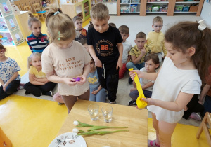 Dziewczynki wkładają do kubka z wodą bibułę.