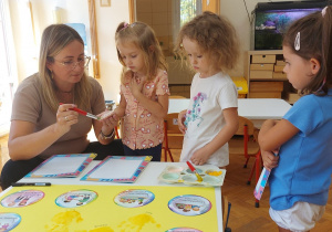 Nauczycielka maluje dłoń dziewczynki farbą w celu odbicia na kodeksie grupowym