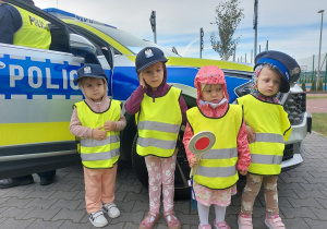 Przedszkolaki pozują do zdjęcia z atrubutami policjanta