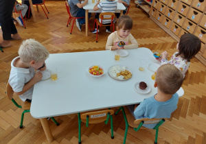 Dzieci siedzaą przy stolikach i jedzą przygotowany poczęstunek