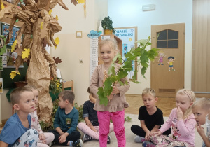 Dziewczynka trzyma w ręku gałązkę z liśćmi klonu.