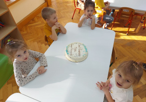 Przedszkolaki siedzą przy stolikach czekając na tort.