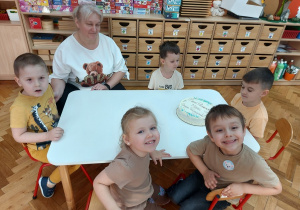 Przedszkolaki z panią siedzą przy stolikach czekając na tort.