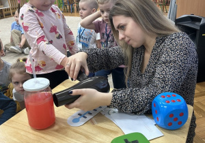 Dziewczynka pomaga pani ogrzać suszarką słoik z czerwoną cieczą