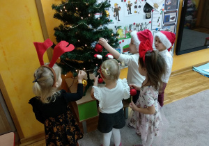 Dzieci wieszają bombki na choinkę.