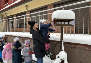 Przedszkolaki dosypują nasiona do karmnika.