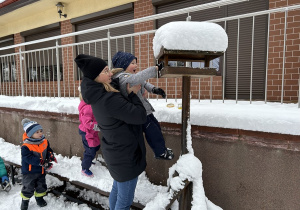 Przedszkolaki dosypują nasiona do karmnika.