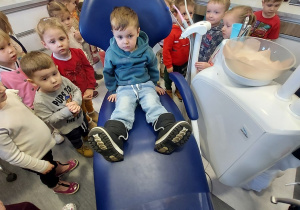 Chłopiec siedzi na fotelu stomatologicznym.