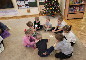 Dzieci w grupach siedzą na dywanie i grają w Dobble