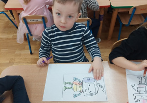 Chłopiec koloruje kredką robota.