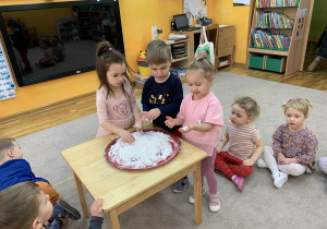 Dzieci próbują zrobić kulki ze sztucznego śniegu.
