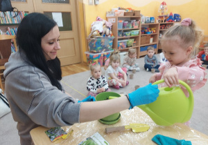 Dziewczynka podlewa konewką zasianą maciejkę.