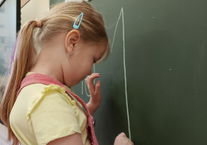 Dziewczynka pisze po tablicy kredą.