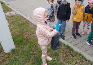Dziewczynka zbiera śmieci z trawnika.