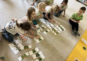 06 Dziewczynki siedzące na dywanie układają puzzle z obrazkiem leprechauna zgonie ze wzorem na tablicy interaktywnej.