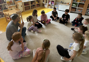 24 Dzieci siedzące w kole na dywanie z nauczycielem podają sobie koszyk z kolorowymi jajkami.
