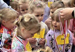 10 Dziewczynki z grupy trzylatków odbierają medale za ukończenie biegu.