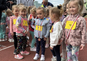 11 Dziewczynki z grupy trzylatków stoją na bieżni z medalami na szyjach.