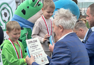 48 Chłopcy z grupy pięciolatków odbierają medale i dyplomy stojąc na podium.