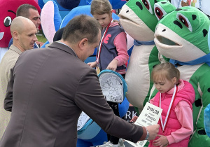 50 Dziewczynka z grupy pięciolatków odbiera brązowy medal i dyplom stojąc na podium.