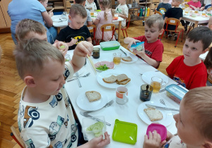 Chłopcy siedzą przy stoliku i robią kanapki.