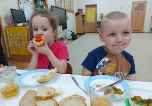 Dzieci siedzą przy stolikach i jedzą kanapki.