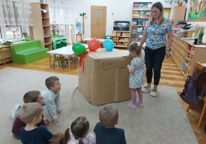 Dziewczynka rozcina nożyczkami zapakowaną w papier niespodziankę