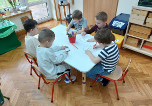 Dzieci siedzą przy stolikach i rysują emocje na przygotowanych szablonach twarzy.