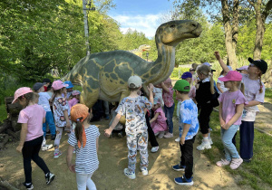 Dzieci głaskają dinozaura.