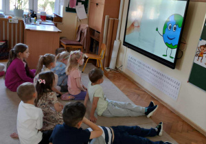 Dzieci oglądają materiał na tablicy multimedialnej.
