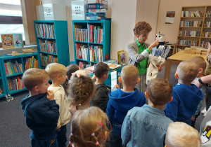 Pani bibliotekarka pokazuje dzieciom upominki w ramach podziękowania za udział w Dyskusyjnum Klubie Książki.
