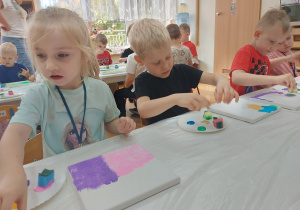 Chłopcy i dziewczynka nanoszą gąbkami farbę na płótna