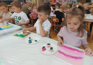 Dzieci przy stolikach malują swoje płótna przy pomocy gąbek