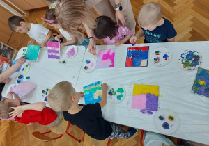 Pani Pleciuga pomaga dzieciom malującym przy stolikach swoje płótna