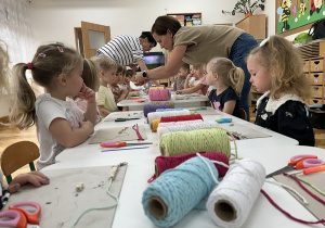 Panie pomagają dzieciom przy stolikach nawlec koraliki na sznurek